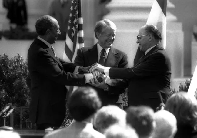 En un apretón de manos con el presidente egipcio Anwar Sadat y el primer ministro israelí Menachem Begin al firmar un tratado de paz en la Casa Blanca.